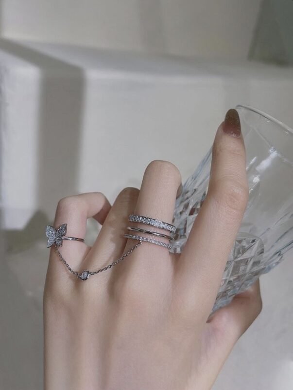 Girls hand holding a glass,, she's wearing silver ring connected from her middle finger to her pinky finger